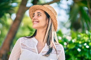 Young hispanic tourist woman wearing summer hat standing at the park.