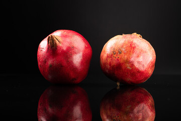 Two red ripe pomegranates on dark background with reflection