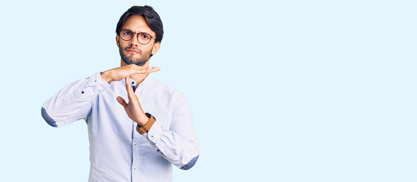 Handsome hispanic man wearing business shirt and glasses doing time out gesture with hands, frustrated and serious face