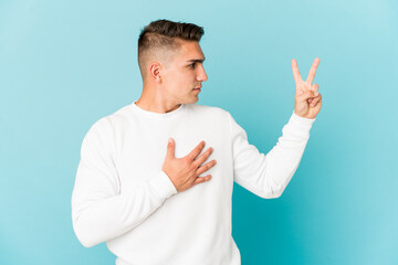 Young caucasian handsome man isolated taking an oath, putting hand on chest.