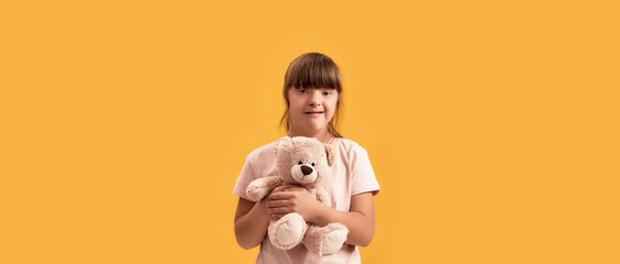 Portrait of disabled girl with Down syndrome smiling at camera, holding her teddy bear while posing...