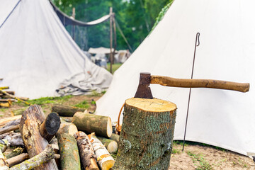 An axe stuck in the stump of a tree with chopped logs at historical reenactment of Slavic or...