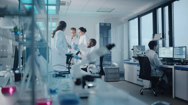 Medical Science Laboratory with Diverse Multi-Ethnic Team of Microbiology Scientists Have Meeting on Developing Drugs, Medicine, Doing Biotechnology Research. Working on Computers, Analyzing Samples