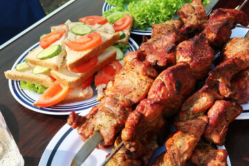 Barbecue skewers on a plate with sandwiches on a wooden table in a park