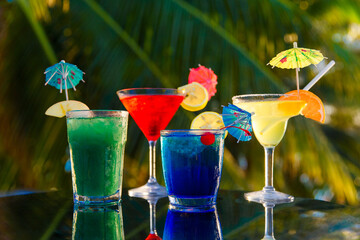 Glasses with colorful cocktails decorated with umbrellas and orange at coconut trees background on...