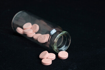 Frasco de cristal abierto y tumbado con pastillas de color rosa sobre un fondo negro