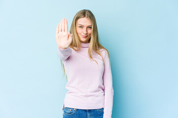 Young blonde woman isolated on blue background standing with outstretched hand showing stop sign, preventing you.