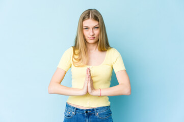 Young blonde woman isolated on blue background praying, showing devotion, religious person looking...