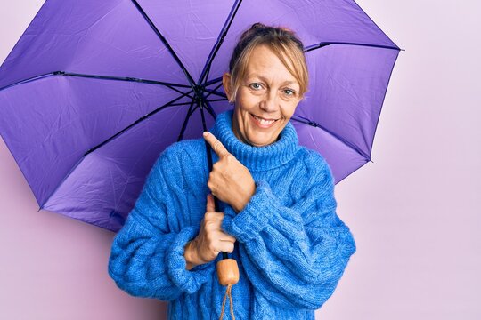 Middle age blonde woman holding purple umbrella smiling happy pointing with hand and finger