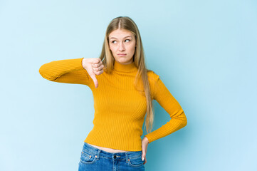 Young blonde woman isolated on blue background showing a dislike gesture, thumbs down. Disagreement...