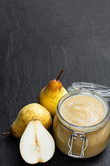 Homemade pear puree in glass jar with fresh ripe pears on black stone background