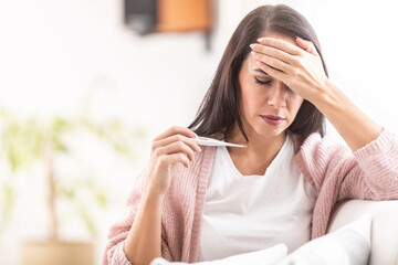 Woman holds her forehead while measuring temperature at home