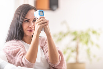 Woman self-measuring temperature with an infrared digital thermometer on her forehead