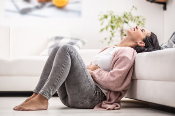 Fototapeta na wymiar Intense menstruation pain freezes a woman sitting on the floor at home