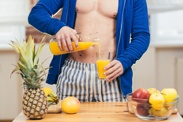 Male athlete, fitness trainer prepares at home juice orange fresh salad