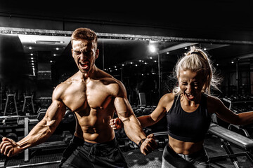 Excited screaming people, muscular man and woman, sportive couple standing in the gym