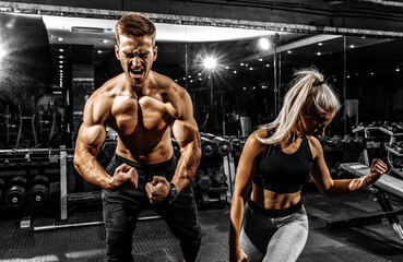 Excited screaming people, muscular man and woman, sportive couple standing in the gym