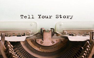 The text Tell Your Story is typed on paper by an antique typewriter. Vintage inscription, retro style, grunge, concept.