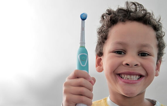 Boy Brushing His Teeth With An Electric Tooth Brush On Grey Background Stock Photo