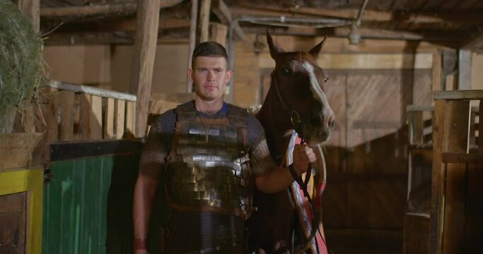 Portrait, a Russian soldier in chain mail leads a horse with a shield and spears. Preparing for battle, the horse is taken out of the stable. 4k, ProRes