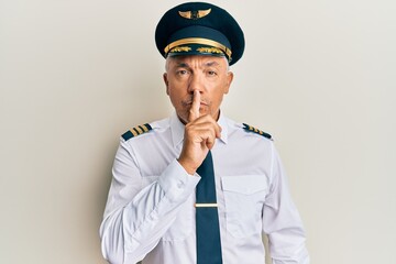 Handsome middle age mature man wearing airplane pilot uniform asking to be quiet with finger on...