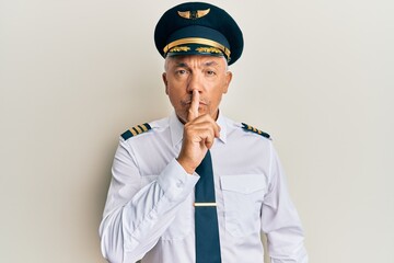 Handsome middle age mature man wearing airplane pilot uniform asking to be quiet with finger on lips. silence and secret concept. © Krakenimages.com