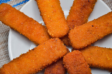 Fish fried sticks on a white plate, on a gray wicker background