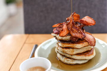 Pancake stack with maple syrup and a large portion of bacon as a breakfast or brunch meal