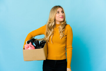 Young blonde caucasian woman holding boxes to move dreaming of achieving goals and purposes