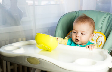 beautiful six months old toddler smeared face with porridge and plays with bowl, concept of feeding...