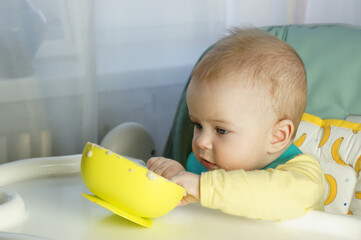 beautiful six months old toddler smeared face with porridge and plays with bowl, concept of feeding...