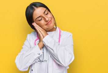 Beautiful hispanic woman wearing doctor uniform and stethoscope sleeping tired dreaming and posing with hands together while smiling with closed eyes.