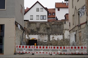 A construction site among houses in the street. It is secured with red and white plastic barrier...