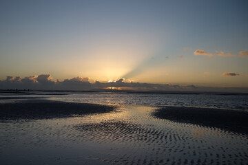 A beautiful sunset and reflections in the water from West Wittering beach with the suns rays bursting over the cloud on the horizon behind the outline of The Isle of Wight.