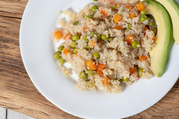 Close-up Quinoa porridge with vegetables and avocado in a white flat plate on a wooden board. Superfoods concept and top view.