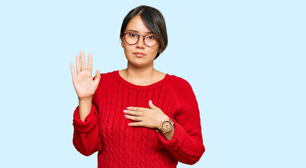 Young beautiful hispanic woman with short hair wearing casual sweater and glasses swearing with...