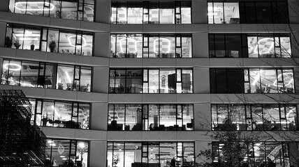 Obraz premium Pattern of office buildings windows illuminated at night. Lighting with Glass architecture facade design with reflection in urban city. Black and white.