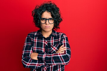 Young hispanic woman with curly hair wearing casual clothes and glasses skeptic and nervous, disapproving expression on face with crossed arms. negative person.