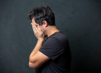 Tired brunet man in black t-shirt on dark background