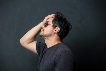 Tired brunet man in black t-shirt and sunglasses on dark background