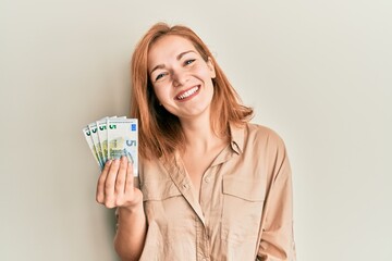 Young caucasian woman holding bunch of 5 euro banknotes looking positive and happy standing and...