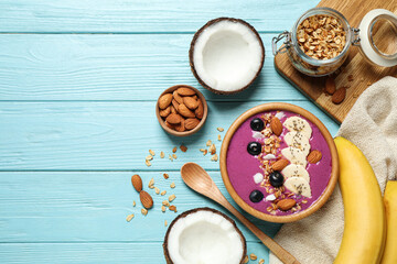 Delicious acai smoothie with granola and almonds served on light blue wooden table, flat lay. Space for text