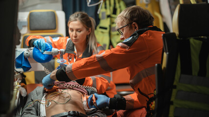 EMS Paramedics Team Provide Medical Help to Injured Patient on the Way to Hospital. Emergency Care Assistants Using a Defibrillator and Ventilation Mask to Bring the Man Back to Life in an Ambulance.