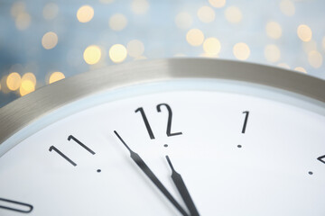 Fototapeta na wymiar Clock on light blue background with blurred lights, closeup. New Year countdown