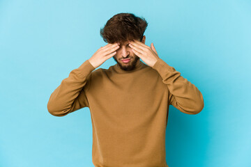 Young arab man on blue background having a head ache, touching front of the face.