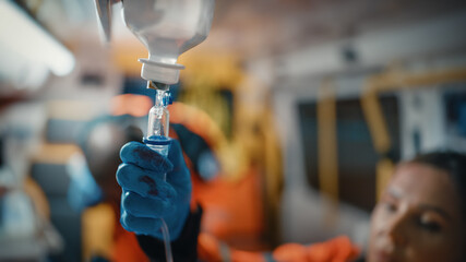 Female and Male EMS Paramedics Provide Medical Help to an Injured Patient on the Way to a Healthcare Hospital. Female Emergency Care Assistant Connecting Intraveneus Line in an Ambulance. Close-up