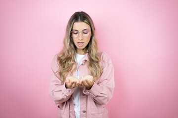 Young beautiful blonde woman with long hair standing over pink background Smiling with hands palms together receiving or giving gesture. Hold and protection