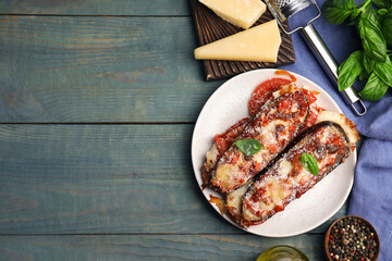 Baked eggplant with tomatoes, cheese and basil served on blue wooden table, flat lay. Space for text