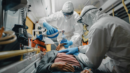 Team of EMS Paramedics in Disposable Coverall Suits Provide Medical Help to Injured Patient on the...