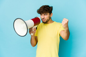 Young arab man holding a megaphone showing fist to camera, aggressive facial expression.